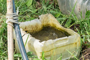 Antik Orta Avrupa köyü, içi opak sıvı, metal boru ve sapla dolu çimenli bir bölge, insan aktivitesi belirtileri, doğal aydınlatma, sessiz renkler, yer seviyesi