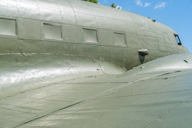 Büyük bir askeri kargo uçağı, zeytin yeşili, asfalta park edilmiş, bulutları dağılmış temiz gökyüzü, ağır yük taşıma modeli, birden fazla kapı, işaret yok, gün ışığı, açık hava sahası veya tesis, insan yok.