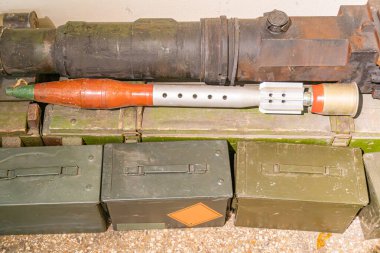 Büyük metalik nesnelerle dolu açık hava sahnesi muhtemelen silah ve istiflenmiş askeri mühimmat sandıkları yeşillik ve metalik palet altında insan, metin veya diğer önemli özellikler yok.