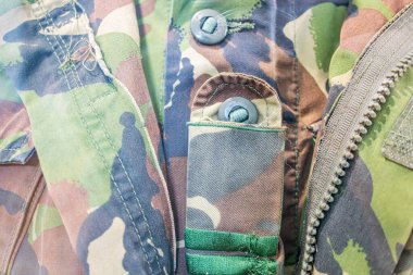 Askeri kamuflaj üniformasının yakın çekim görüntüsü, kahverengi ve yeşil desenli pürüzlü kumaş ceket ya da giysi kapanışına işaret eden görünür düğmeleri var insan figürleri ya da diğer nesneler yok.