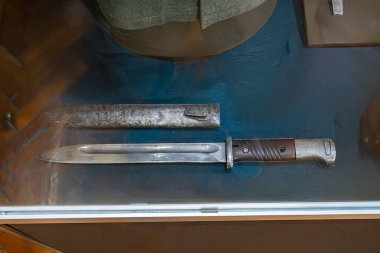 Vitrinde klasik çift namlulu tüfek, paslı ve lekeli eski metalik yüzeyler, ahşap stok, yumuşak gölgeler, kahverengi ve gümüş palet