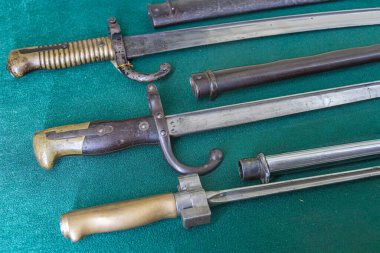 Koyu yeşil bir yüzey üzerinde iki sıra halinde dizilmiş sekiz kılıçtan oluşan bir kolleksiyon üst satırda farklı dizaynlara sahip dört büyük kılıç ve alt satırda dört küçük sl bulunur.