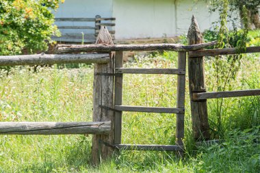 Kırsal, basit bir çit içindeki ahşap kapı, ötesinde çimenlik alan, arka planda potansiyel kırsal bina veya ahır, öğleden sonra aydınlatma, sessiz renkler, doğal stil.