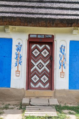 Ağır dekore edilmiş mavi kapı ve basit pencerelerle donatılmış, parlak gün ışığı altında kuru bir ortamda kurulmuş geleneksel bir Orta Avrupa binası.