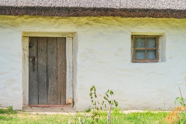 Orta Avrupa 'da bir köyde dikey ahşap kapılı ve yan pencereli küçük, beyaz sazdan bir ev. Bulutlu bir gün ortamı, yeşillik ve bahçe manzarası, yüksek perspektif.