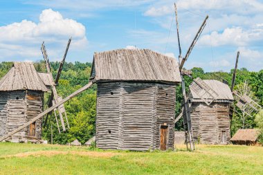 Çoklu ahşap yel değirmenli kırsal Orta Avrupa köyü, yemyeşil bir zemin ve berrak gökyüzü ahşap yapı, eğimli çatılar, çoklu yelkenler, yuvarlak üsler, potansiyel s