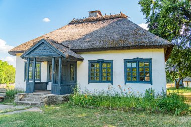 Eski Orta Avrupa evi, mavi aksanlı, sazdan çatı, baca, basamaklar, yemyeşil, kır çiçekleri ya da süs bitkileri, gündüz vakti, güneş ışığı, açılı perspektif, insan ya da hayvan yok.