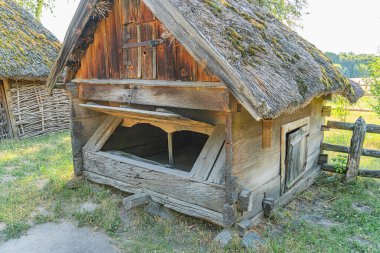 Eski, yıpranmış bir ahır Orta Avrupa kırsalında gündüz vakti bulutlu bir gökyüzü altında dikey ahşap döşeme ve aşınmış çimen ve ag işaretleri gösteren bir çatı geleneksel tasarımı