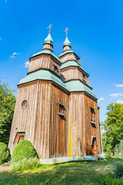 Orta Avrupa köyündeki antik ahşap Ortodoks kilisesi, yıpranmış ahşap, birden fazla kule, haçlar, huzur ortamı, yeşillik, temiz mavi gökyüzü, insan yok, gün ışığı, canlı renkler, dokular, kemer