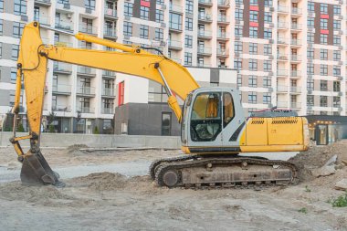 İnşaat alanındaki sarı buldozer, balkonlu konuma yakın bir yerde. Öğleden sonra aydınlatması günbatımını gösteriyor. Belirgin bir işaret ya da metin yok.
