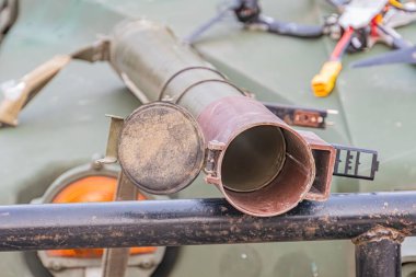 Askeri araç bileşeninin yakın görüntüsü, muhtemelen silindirik silindirik tasarımı ve eşleştirilmiş yeşil-gri renk paleti ile APC parçası, atölyede yapay ışıklandırma veya kontrollü çevre