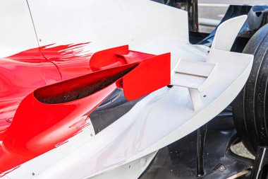 Beyaz ağırlıklı kırmızı aksanlı ve siyah detaylı, muhtemelen karbon fiber gibi hafif malzemelerden yapılmış bir Formula 1 aracının yan görüntüsü.