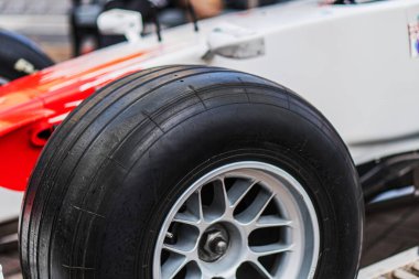 Monitörde tek bir Formula 1 yarış arabası tekerleği var, vida ve fındıklı çoklu konuşma tasarımı, arka planda kısmen görünür beyaz ve kırmızı araç gövdesi, yumuşak gölgeler, üstten aydınlatma