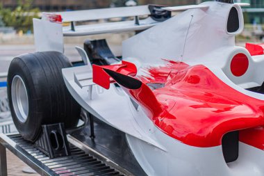 Durgun Formula 1 arabası pit lane standında, ağırlıklı olarak beyaz, kırmızı ve siyah aksanlı, ön kanat alev dizaynını taklit ediyor, 7 numara görünür, arka plan bulanık yarış ekipmanları, insan yok.
