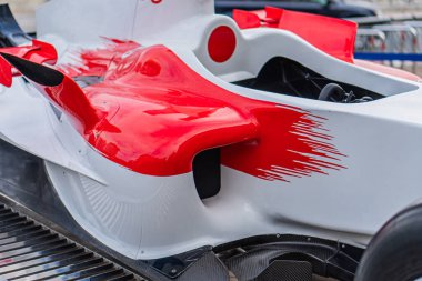 Formula 1 yarış arabasının yakın çekimi ağırlıklı olarak beyaz ve kırmızı renkte, aerodinamik tasarım sergiliyor. Rüzgâr yönünü taklit ediyor. Bulanık arka plan hızı ve hareketi arttırıyor.