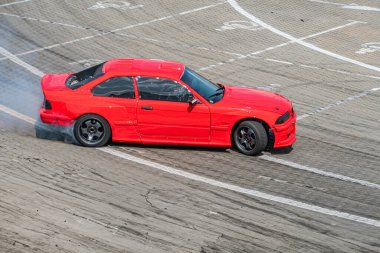 Pistte yarış arabası, canlı kırmızı vücut açılı, beyaz işaretli gri yol, bulutlu aydınlatma, gizli stil, yükseltilmiş kenar açı