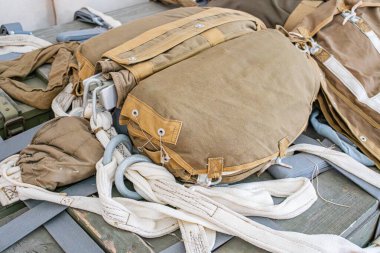 Tahta bir yüzeyde askeri paraşüt koleksiyonu, kayışlı ve tokalı kahverengi renk, dağınık ışıklandırma, kapalı alan ortamı, üst perspektif, gerçekçi stil.