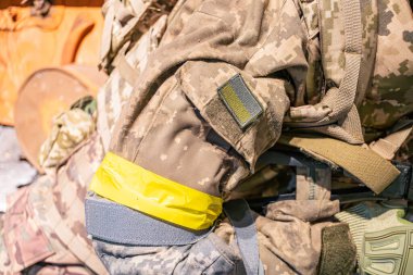 Zeytin yeşili, sarı şeritli bir askeri bandın yakın çekimi, muhtemelen güvenlik teçhizatı, dış plan bulanıklığı, etiketten süzülen doğal ışık, ama okunamıyor.