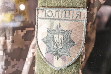 Kolunda Kiril amblemi olan Ukrayna askeri polis üniformasının yakın çekim görüntüsü bir kalkan, defne çelengi, Kiril alfabesi metni ve ilavelerden oluşuyor.