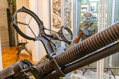 Görüntü, askeri teçhizat odaklı bir iç ayarı resmediyor, bir standın üzerine yerleştirilmiş büyük, yıpranmış bir döner top tarihi bilgi içeren yeşil bir tahta içeriyor