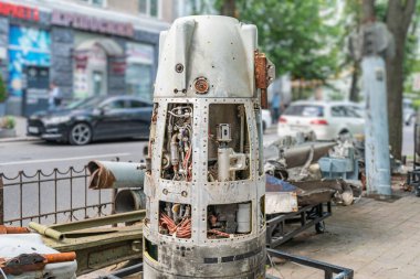 Eski, paslı metal bir roket parçası, muhtemelen bir tank ya da motor, bir tuğla binaya karşı bir şehir ayarında tasvir edilir. Sahne ağaçlar, beton kaldırımlar, park edilmiş arabalar ve kırmızı bir tabela içerir.