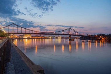 Gece vakti nehir manzarası, aydınlatılmış köprü ve binalar.