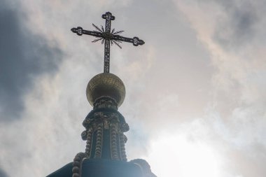 Koyu taştan kilise kubbesi, üzerinde çapraz kubbe olan gri bulutlar arasından süzülen güneş ışığı gölgeler oluşturur ve aşağıdan ayrıntılı bir perspektifin altını çizer.