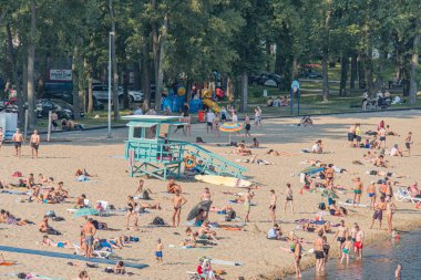 Kyiv, Ukrayna 'da canlı plaj sahnesi dinamik gölgeler, kırmızı beyaz cankurtaran standı, kumlu kıyılara dağılmış insanlar, canlı renklerde şemsiyeler Kyiv, Ukrayna 07-04-2025
