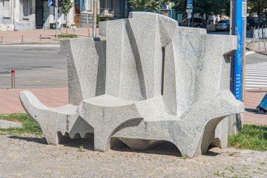 Kumlu zemindeki modern soyut heykel, düzensiz bloklardan oluşmuş, organik kaya oluşumlarını veya insan duruşunu anımsatan oturma alanları oluşturmaktadır. Renkler Kyiv, Ukrayna 07-06-2025