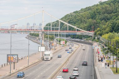 Sunrisesunset 'teki Kyiv şehri, karışık trafiği, canlı renkleri, yemyeşil suyolu, görkemli su yolu, modern binalar, asma köprü Kyiv, Ukrayna 07-06-2025