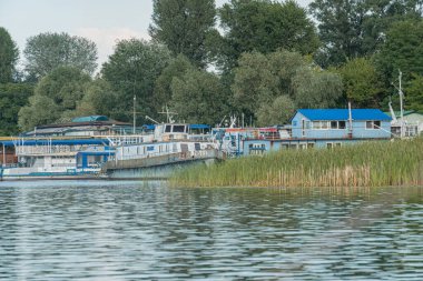 Ukrayna 'nın başkenti Kyiv' deki bulutlu marina sahnesi kıyıya demirlemiş birkaç tekne çevreleyen yeşillik ve sakin su Kyiv, Ukrayna 07-12-2025