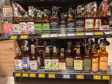 Bir alkol dükkanında metal içki rafı görüntüsü, farklı şekil ve boyutlarda etiketlenmiş çeşitli şişeler taşıyor, çevredeki yumuşak ışık altında Dünya tonları Kyiv, Ukrayna 07-12-2025