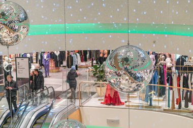 Modern tasarımı olan mağaza, yeşil beyaz tavan, küresel avizeler, fayans döşemeleri, yürüyen merdivenler, mankenler, şık kıyafetler, alışveriş yapanlar, kentsel iletişim Kyiv, Ukrayna 12-24-2023