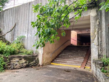 Sanayi merdiven boşluğu merkezi, tepedeki bir açıklıktan geçen doğal aydınlatma, beton bir duvarda bitki örtüsü ve eski taş duvarlar, düz bir bakış açısı, gün ışığı ortamı.
