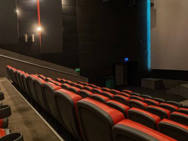 Az ışıklandırılmış VIP sinema salonu, kırmızı koltuklar, bazı yerlerde bulanıklaşma, geniş ekran görüntüleme içeriği ile sahne alanına odaklanma Candid tarzı yakalama olayı ya da sonuç: