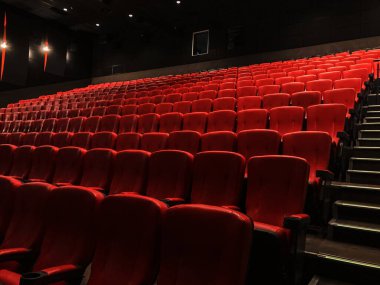 Kırmızı koltuklar, tavan ışıkları ve yumuşak gölgelerin yer aldığı boş bir VIP sinema salonunun yakın görüntüsü kırmızı ve beyaz renk şeması