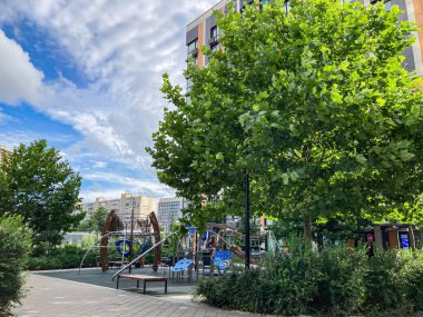 Güneşli bir gün parkı sahnesi, slaytlı çocuklar oyun alanı, dağcılık çerçeveleri mavi plastik sandalyeler yemyeşil ağaçlar, parlak, bulutsuz