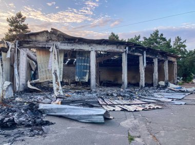 Yanmış bir dükkan, yanmış bir dış mekan, kısmen çökmüş bir yapı, açığa çıkmış çatı ve iç döküntüler, yanmış odun, açık alan, gölgeler, öğleden sonra aydınlatması, insan ya da hayvan yok.,