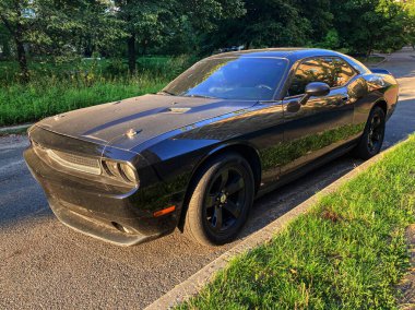 Siyah, yüksek performanslı güçlü araba, açılı, parlak tasarım, parlak dış görünüş, renkli pencereler, tekerlek kemerleri, kas hatları, yerleşim sokağı, yeşillik, sıcak aydınlatma, sabah erken ya da geç saatlerde, c