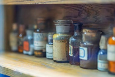 Cam şişeler ve kavanozlarla dolu klasik ahşap eczane rafı, yumuşak ışıklandırma, kırsal ortam, doğal renkler.