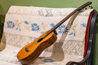 Klasik bir akustik gitar çiçek desenli bir mobilya parçasına çapraz olarak yerleştirilir, sessiz tonlu bir duvara karşı, gitar parlak bir kapanışa ve ses etrafında dairesel detaylara sahiptir.