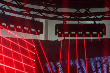 Lazer şovlu gece kulübü sahnesi, siyah metal iskele, canlı kırmızı ve mavi ışıklandırma, DJ, hoparlörler, ek olarak asılı aydınlatma armatürleri.