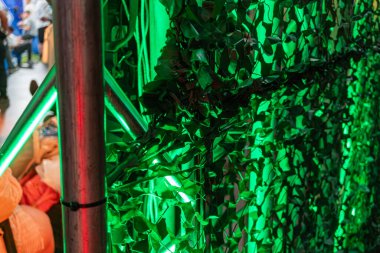 Delikli büyük yeşil ağ duvar, kırmızı ve beyaz silindirik nesneler, farklı boyutlarda ve konumlarda, sağ taraftan aydınlatma, çarpıcı gölge etkisi yaratır.