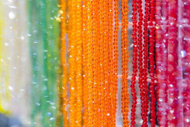 Kırmızı, portakal, sarı ve yeşillik üst üste binen sicimlerdeki ışığı yansıtan sıcaktan serin renklere geçişi olan birden fazla iplikçikli renkli, eşit kesimli değerli boncukların yakın çekimi
