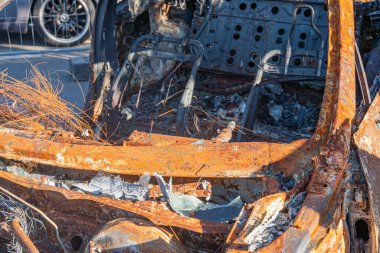 Yanmış araba enkazı kömürleşmiş metal, bükülmüş çerçeveler ve dağınık kül kalıntıları, siyah ve gri renk paleti, aşağı doğru perspektif