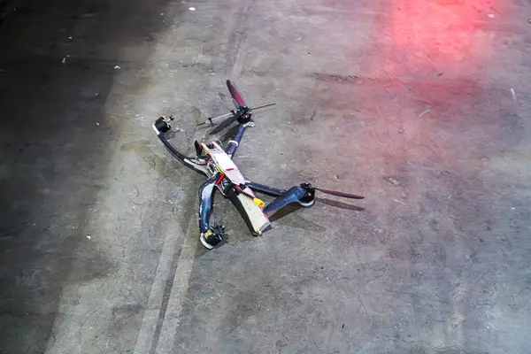 Dört pervaneli siyah bir dron desenli beton zeminde uzanıyor İHA 'nın elektronik bileşenleri, bir anten ya da kamera montajı var ve yandan markalaştırma yok.