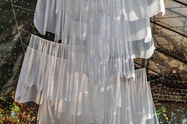 Fırfırlı yüzen iki beyaz şemsiye, açık bir gökyüzü altında asılı, yukarı doğru perspektif, minimalist stil ve gölge oyunu vurguluyor