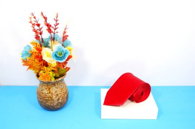 Çiçek vazosuyla birlikte beyaz hediye kutusuna sarılı kırmızı bir kravat. 