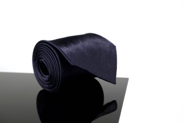 Yansıma cam yüzeyi üzerinde siyah bir kravat yuvarlanmış. Yakından tek bir nesne görüntüsü. 