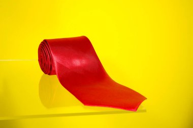 Kırmızı kravat cam yüzeyde yuvarlandı. Sarı arkaplan ile yakın plan görüntüsü. 